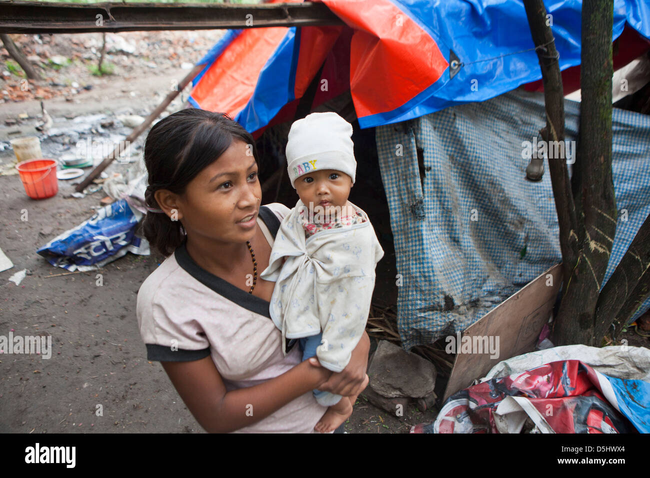 Una giovane madre Nepalese trattiene il suo bambino al di fuori della loro tenda di plastica home in Nazioni Unite Park, una delle baraccopoli in Paurakhi Basti, Nepal. Foto Stock