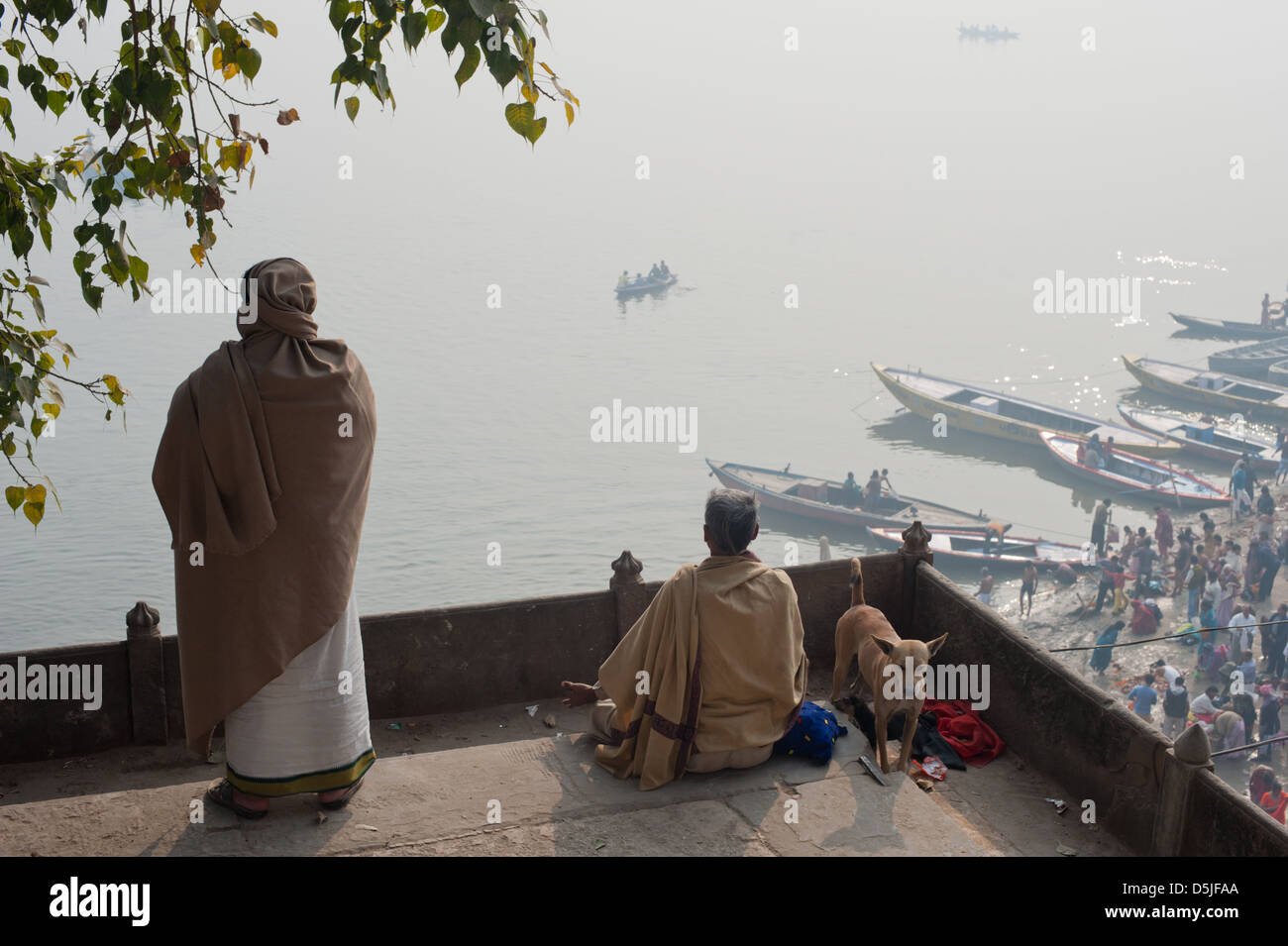 Un uomo orologi mentre un altro medita, il primo giorno del Kumbh Mela, Varanasi (India). 2013 Foto Stock