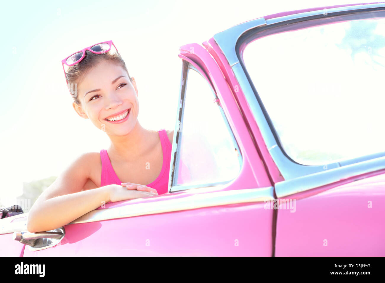 Bella multirazziale caucasico Cinese / Asian sorridenti giovane donna in auto rosa andando sul viaggio sul giorno di sole Foto Stock