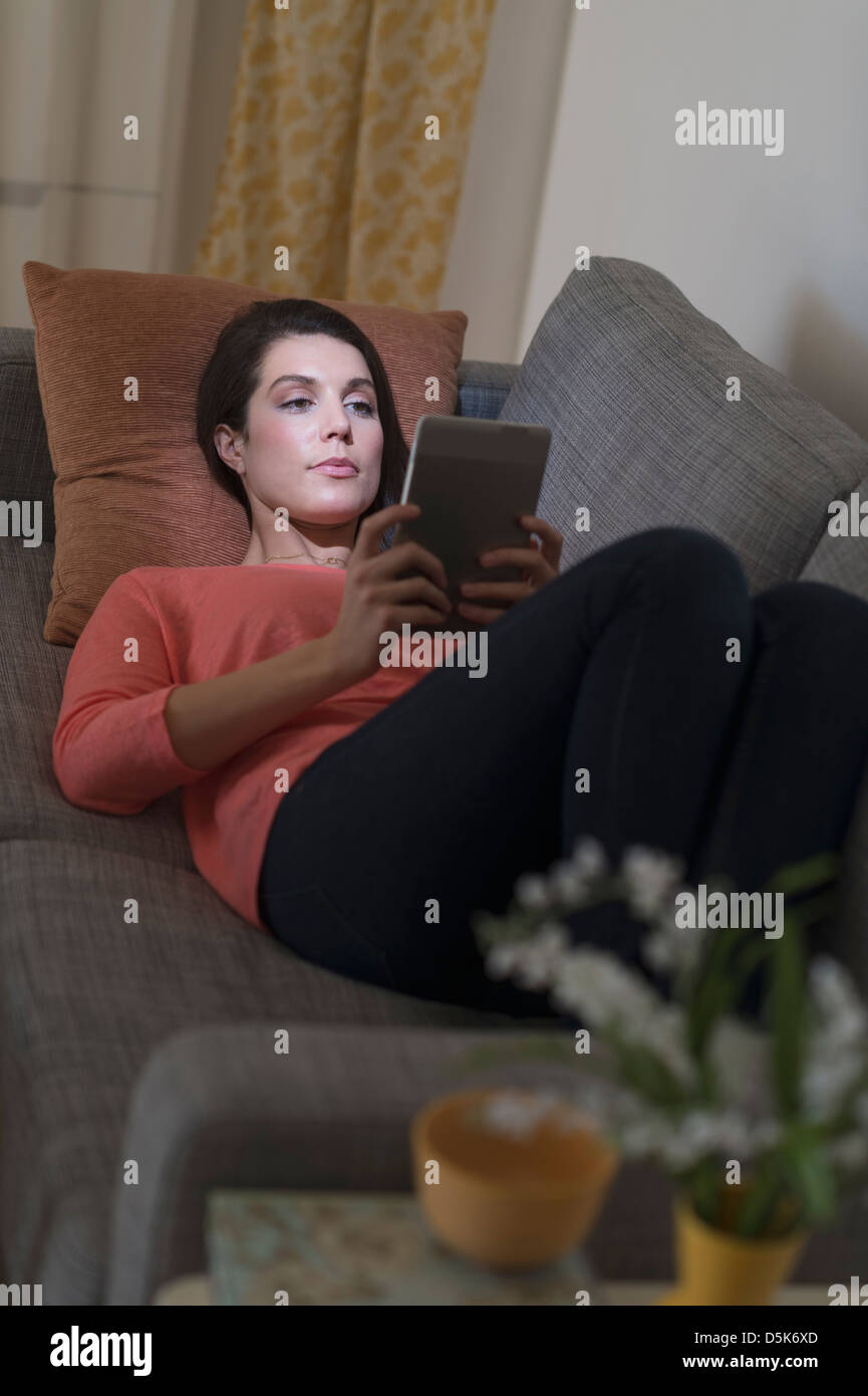 Donna che utilizza digitale compressa mentre sdraiato sul divano Foto Stock