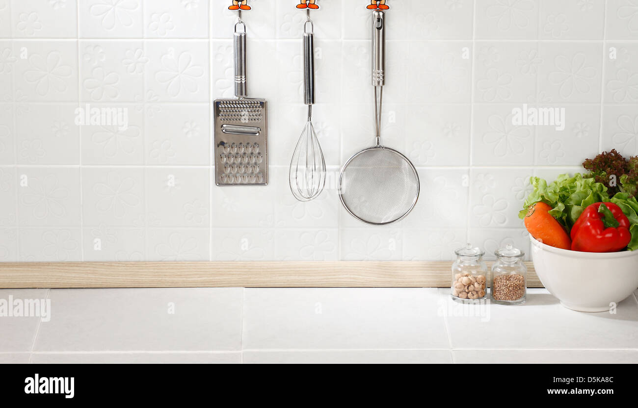 Cucina utensili di cottura sul gancio contro la parete di piastrelle Foto Stock