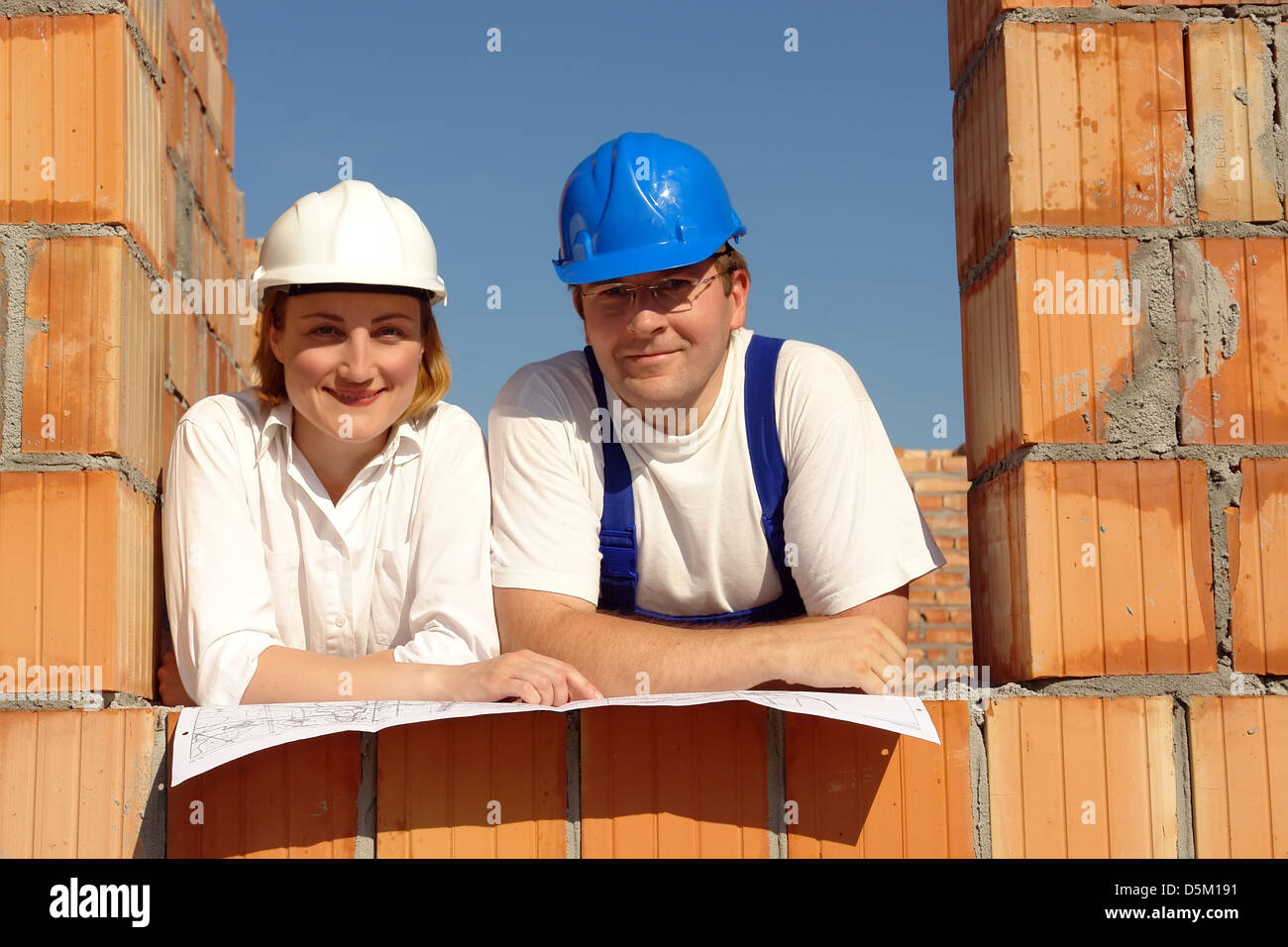 Paio di indossare copricapi rigidi in posa nella loro futura casa di apertura della finestra in appoggio sul piano di costruzione Foto Stock