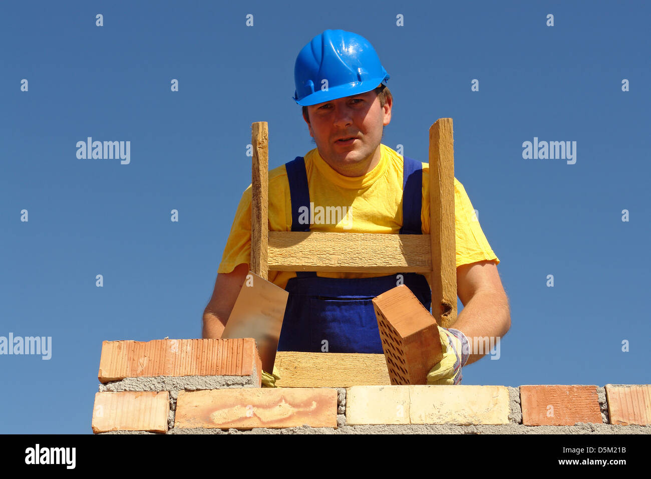 Mason nel casco blu la costruzione di un muro di mattoni Foto Stock