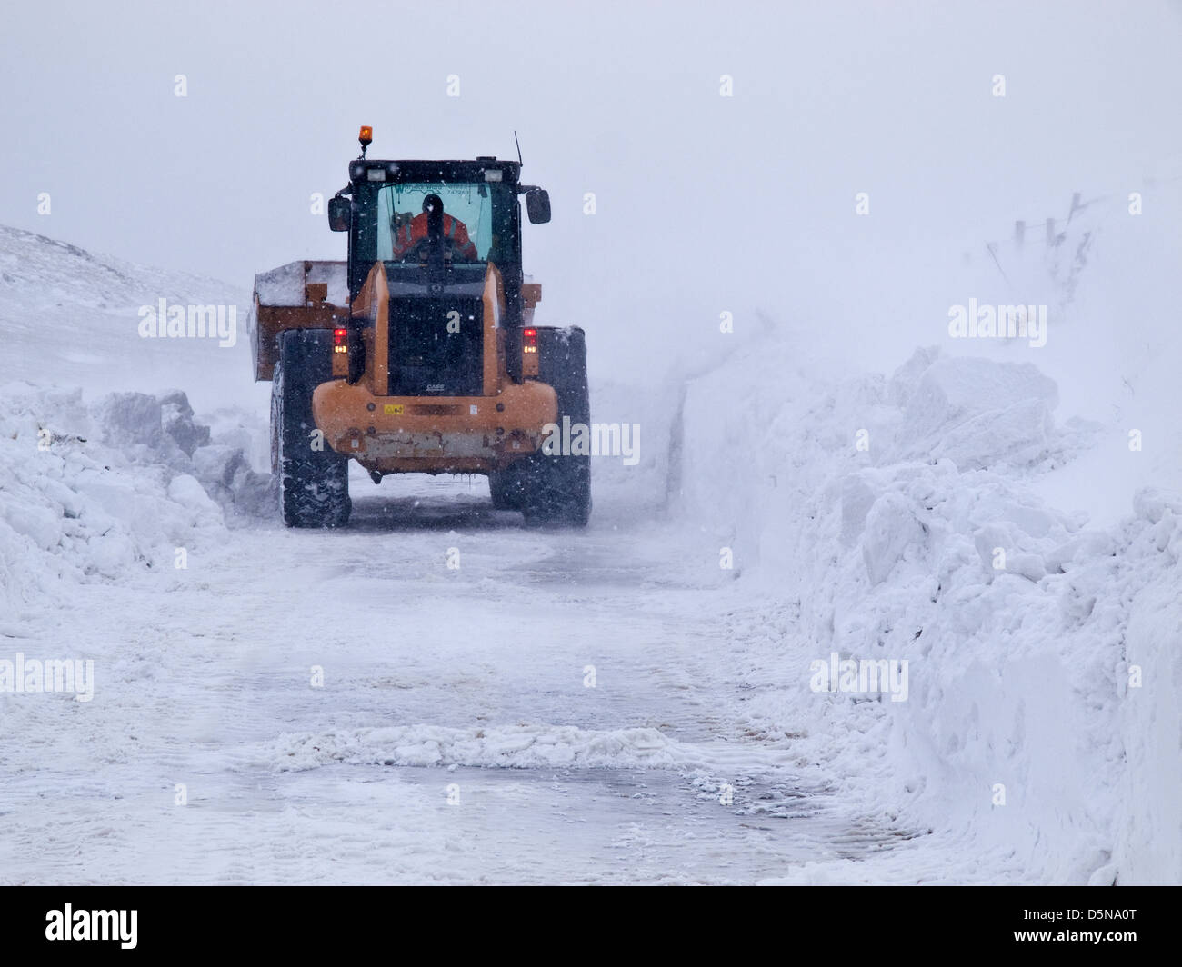 Un trattore / digger cercando di mantenere un Peak District road aperto in presenza di un notevole manto di neve durante l'inverno del 2013 Foto Stock