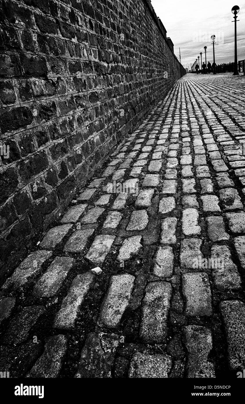 Strada di ciottoli con un muro di mattoni e lampioni in Liverpool, UK. Foto Stock
