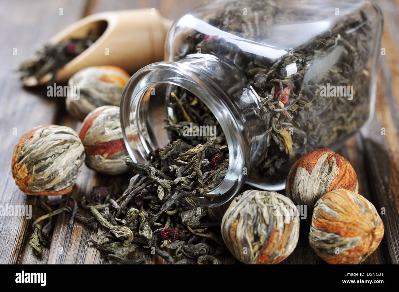 Il tè verde sfere con fiori e vaso di vetro con tè sul tavolo di legno Foto Stock