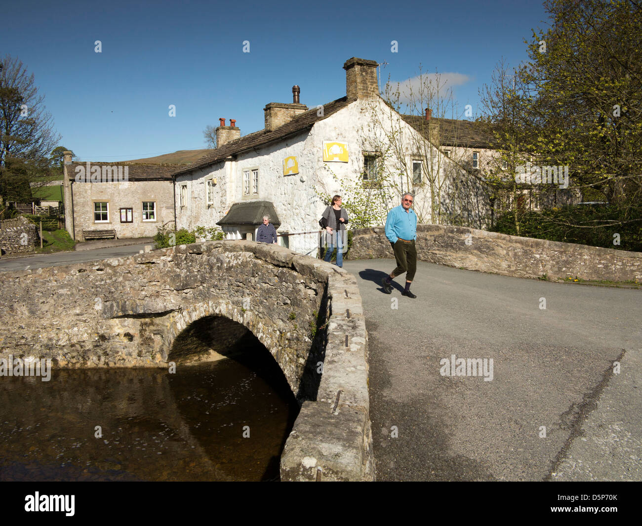 Regno Unito, Inghilterra, Yorkshire, Malham, walkers attraversando il vecchio ponte di pietra sul fiume Aire Foto Stock