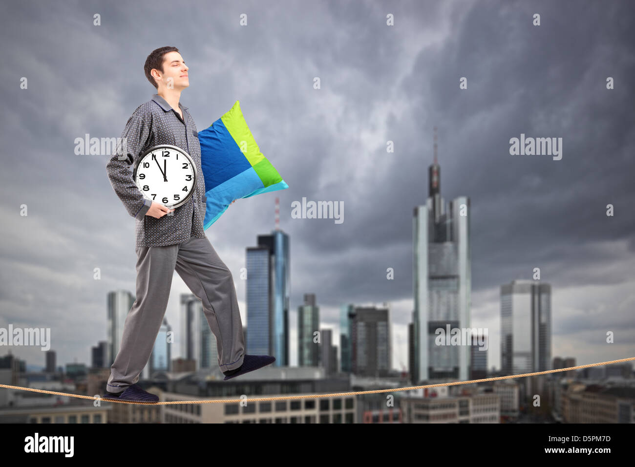 Un uomo in pigiama tenendo un cuscino e orologio sonnambulismo su una fune, con il centro finanziario di Francoforte, Germania Foto Stock