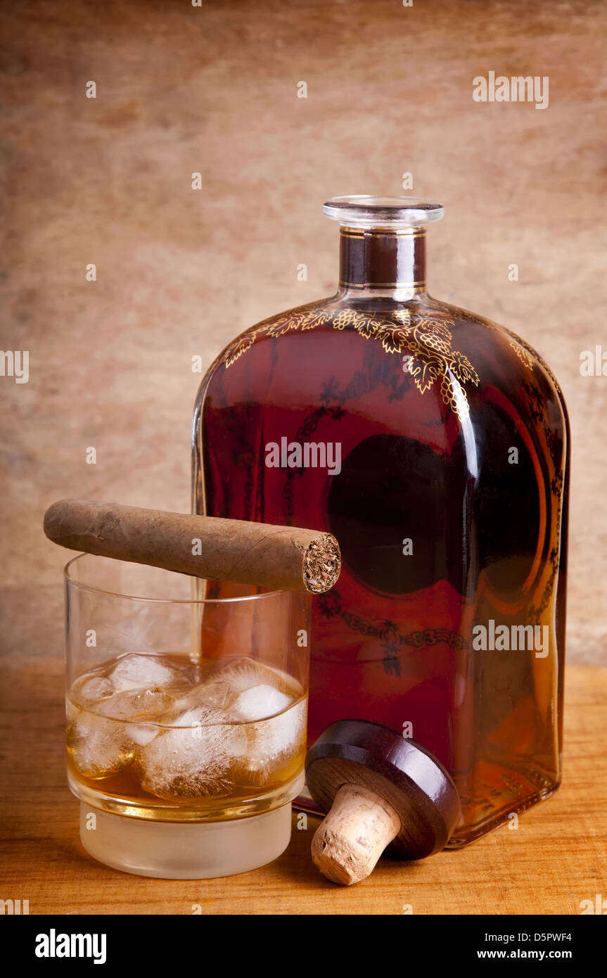 Vetro e bottiglia di whiskey con sigaro cubano su uno sfondo di legno Foto Stock