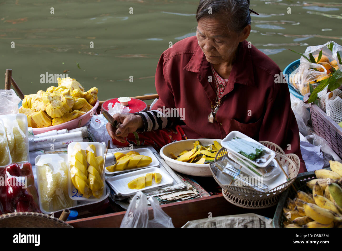 Vecchia donna tailandese di vendita di alimenti da la sua barca al mercato galleggiante in Thailandia Foto Stock