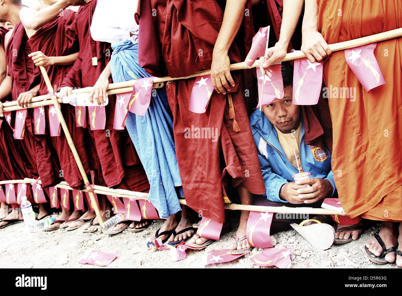 Un uomo si siede tra schiere di monaci buddisti, durante l'attesa per l arrivo di Aung San Suu Kyi, in occasione di una visita a Mandalay. Foto Stock