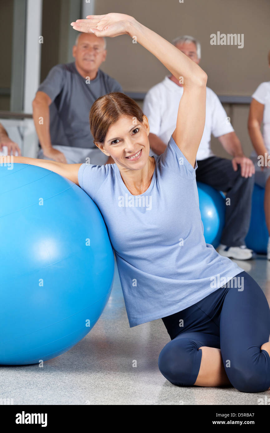 Donna sorridente facendo esercizi per la schiena con palla nel centro fitness Foto Stock