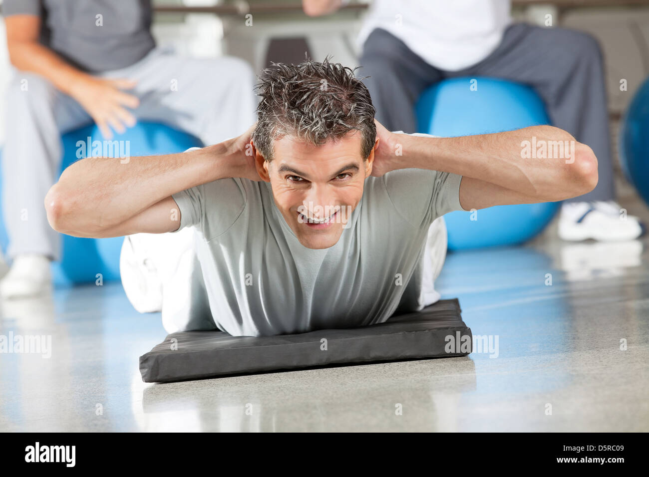 Uomo felice facendo esercizi per la schiena sul tappetino palestra nel centro fitness Foto Stock