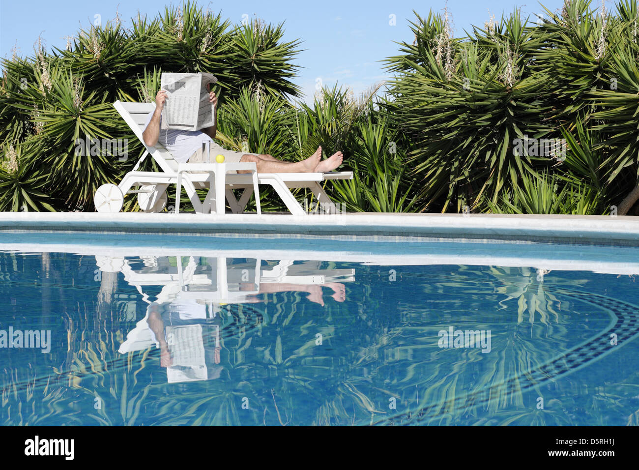 L'uomo rilassante sulla tranquilla piscina e quotidiano di lettura Foto Stock