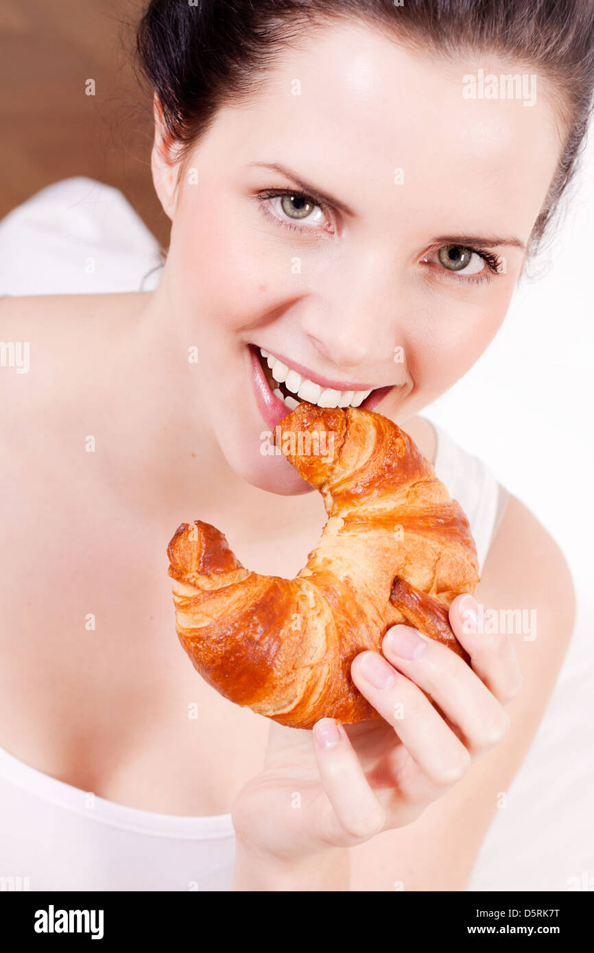 Donna sorridente ritratto di mangiare un cornetto per colazione Foto Stock