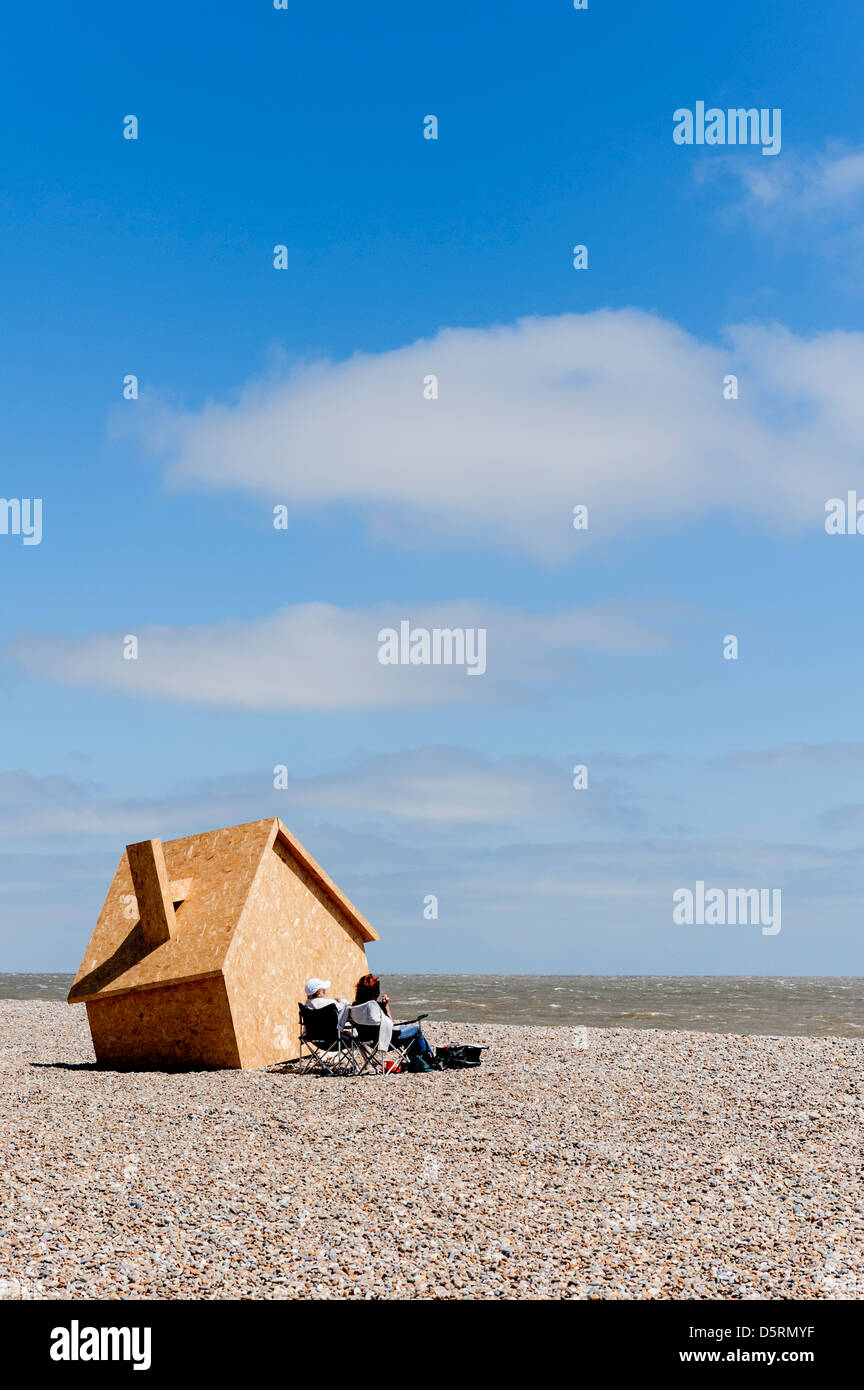 Due persone sedute accanto a un moderno in legno arte scultura della casa tra le nuvole sulla spiaggia Thorpeness nel Suffolk. Foto Stock