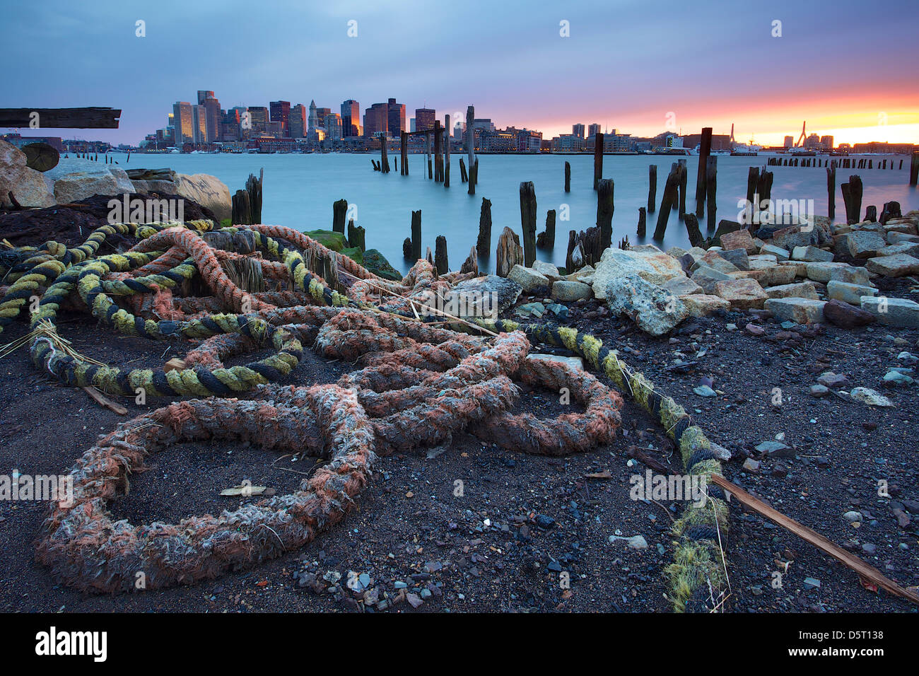 Strappati fune su un molo abbandonato lungo il Porto di Boston con lo skyline della città in background. Foto Stock