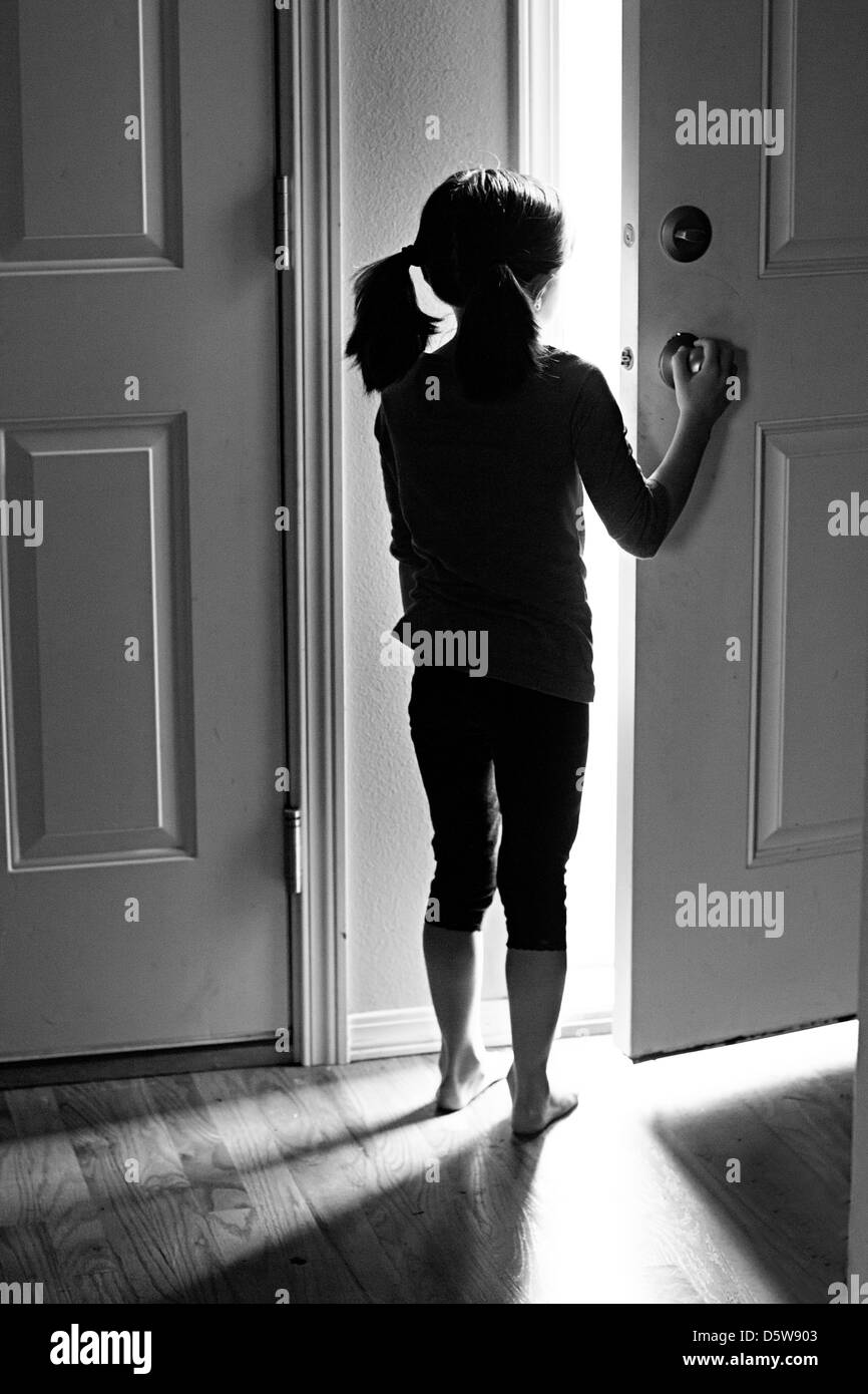 Una ragazza si affaccia una porta, bagnata in ombra e luce Foto Stock