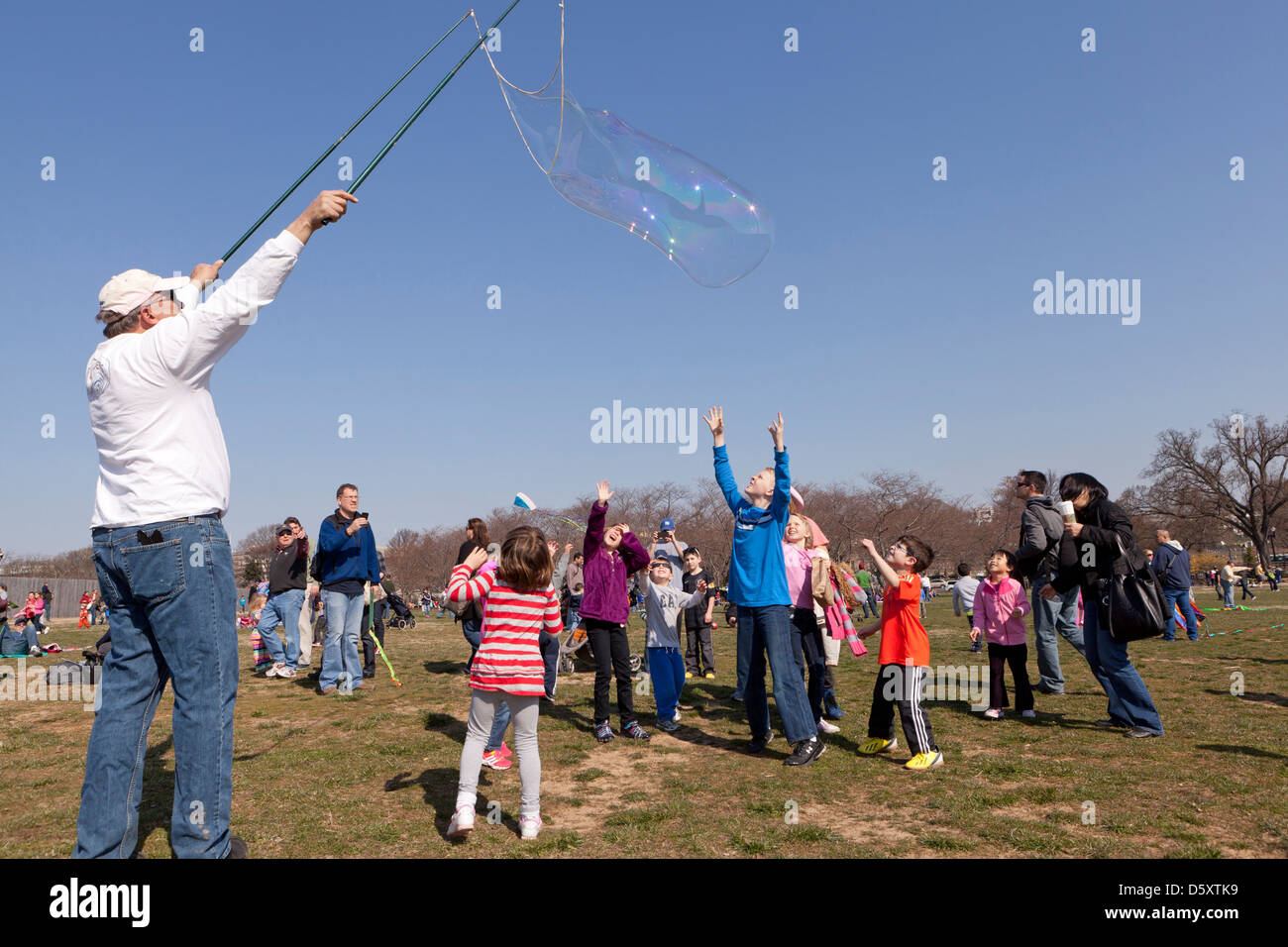 Uomo anziano rendendo le bolle più grandi per i bambini nel parco Foto Stock
