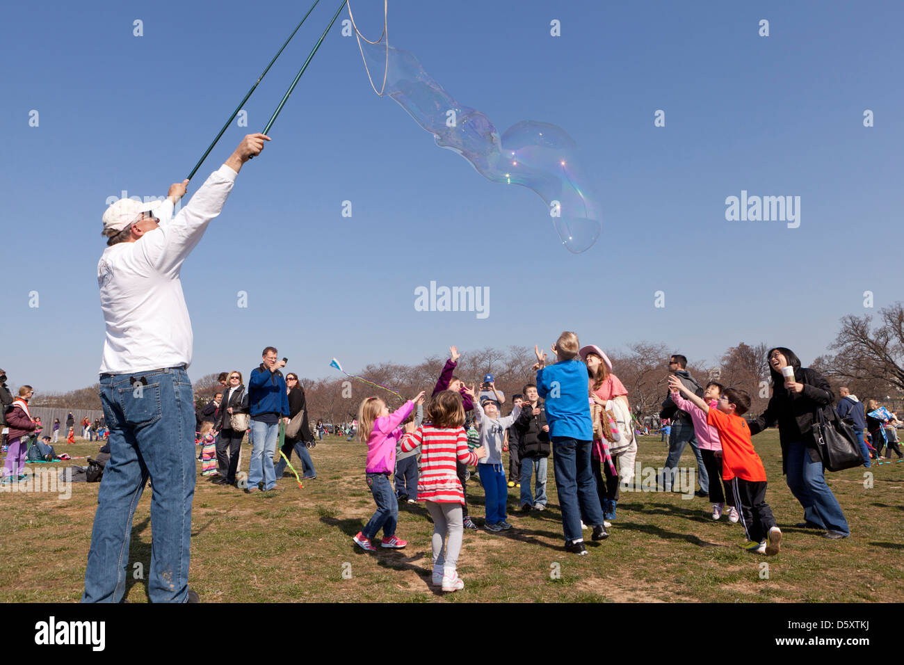 Uomo anziano rendendo le bolle più grandi per i bambini nel parco Foto Stock