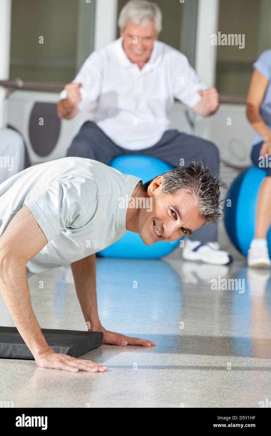 Uomo sorridente facendo push up nel centro fitness sul tappetino palestra Foto Stock