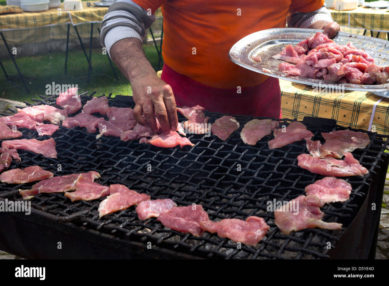 L'uomo immissione pezzi grezzi di carne su un barbecue esterno grill Foto Stock