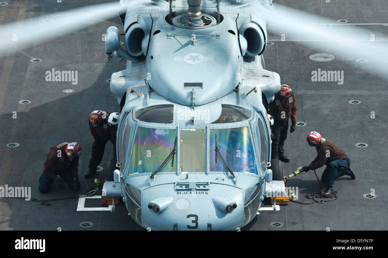 US Navy marinai guarnitura e catena un MH-60S Knight Hawk elicottero sul ponte di volo della portaerei USS Nimitz Aprile 4, 2013 nell'Oceano Pacifico. Foto Stock