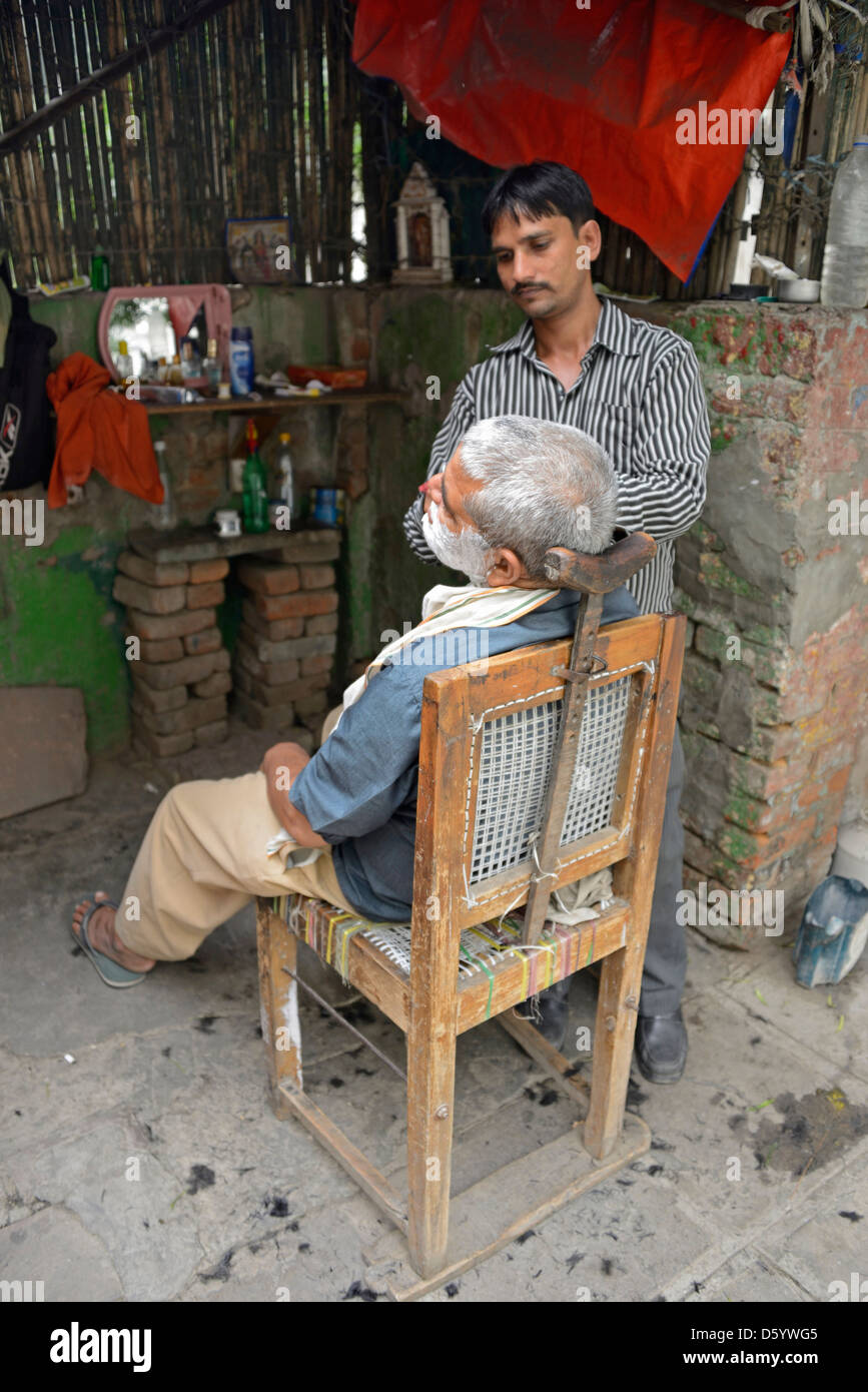 Un cliente avente una faccia di rasatura nel realizzare localmente un negozio da barbiere in una strada laterale di Nuova Delhi in India Foto Stock