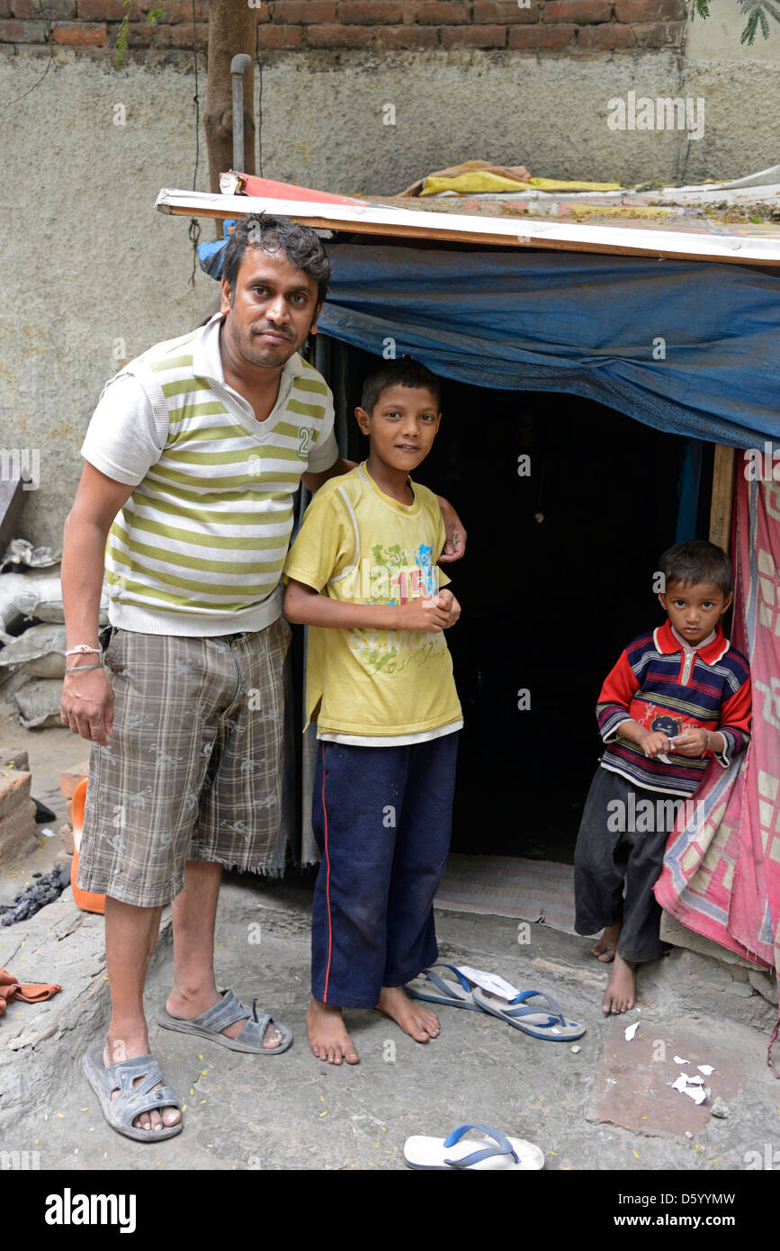 Un orgoglioso padre e i suoi due figli davanti alla porta della loro casa di fortuna in una strada laterale di Nuova Delhi in India Foto Stock