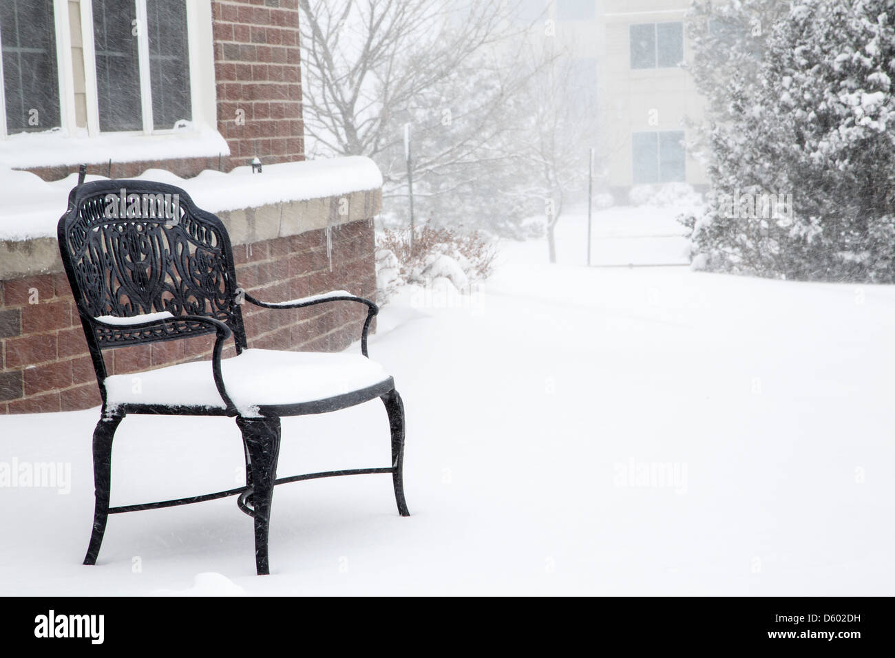 Un vuoto, nero, ferro battuto banco in una tempesta di neve da un edificio in mattoni Foto Stock