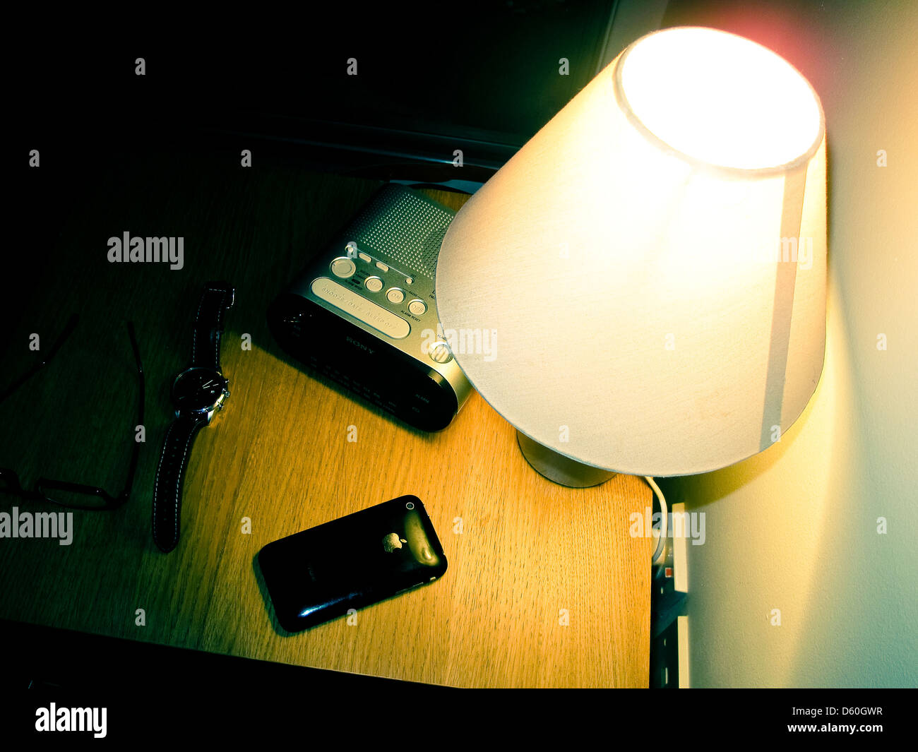 Comodino con lampada radiosveglia bicchieri e iPhone Foto Stock