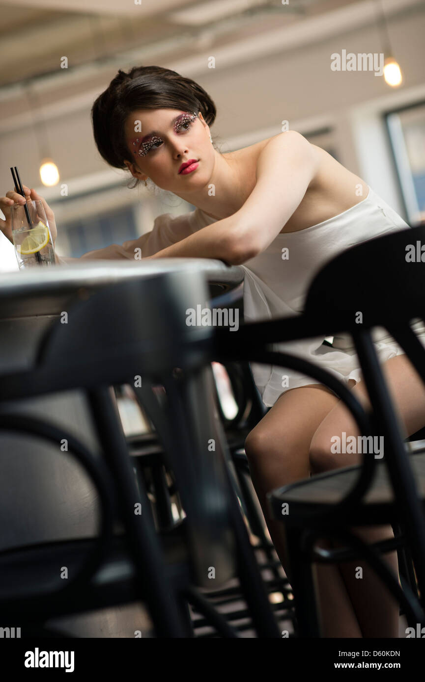 Una giovane e bella donna ragazza adolescente con anni sessanta lo stile dei capelli, vestiti e trucco, big ciglia, seduto in un bar REGNO UNITO Foto Stock