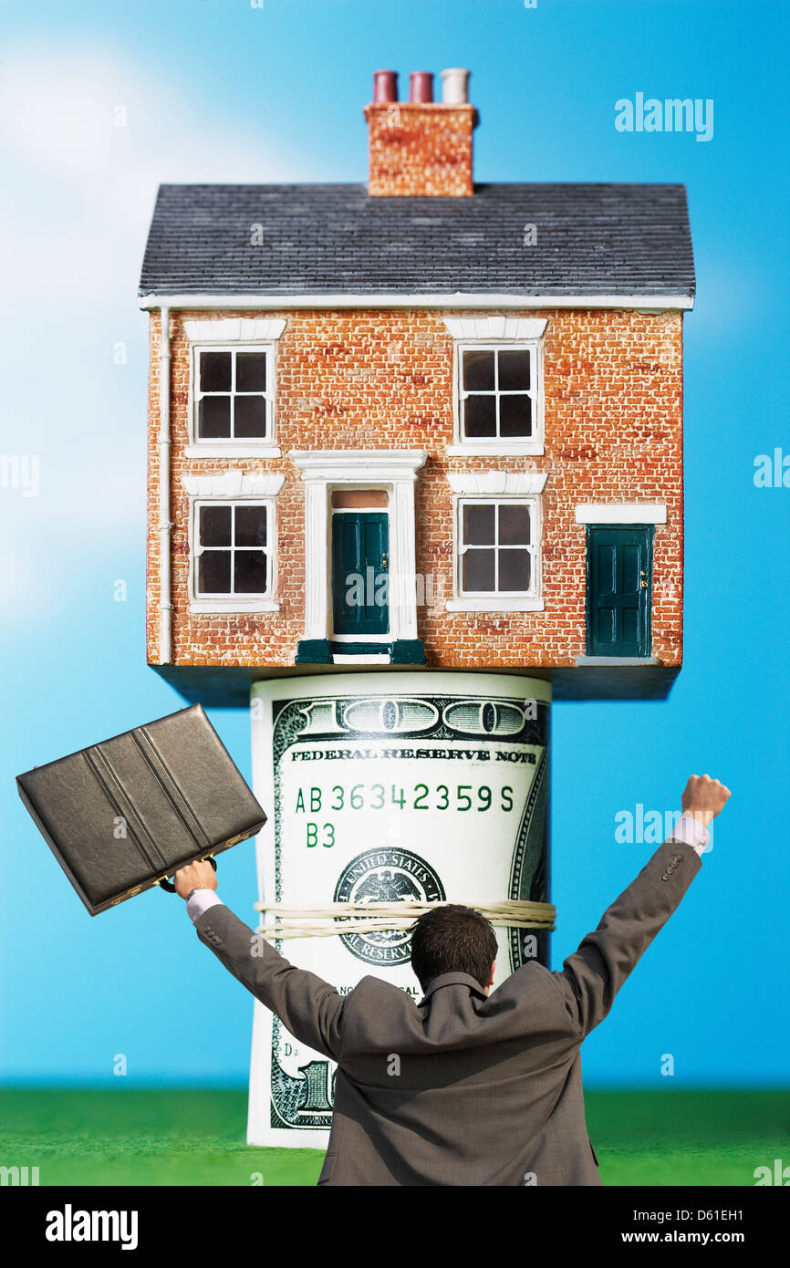 Vista posteriore del businessman vittorioso con valigetta di fronte casa denaro rotoli Foto Stock