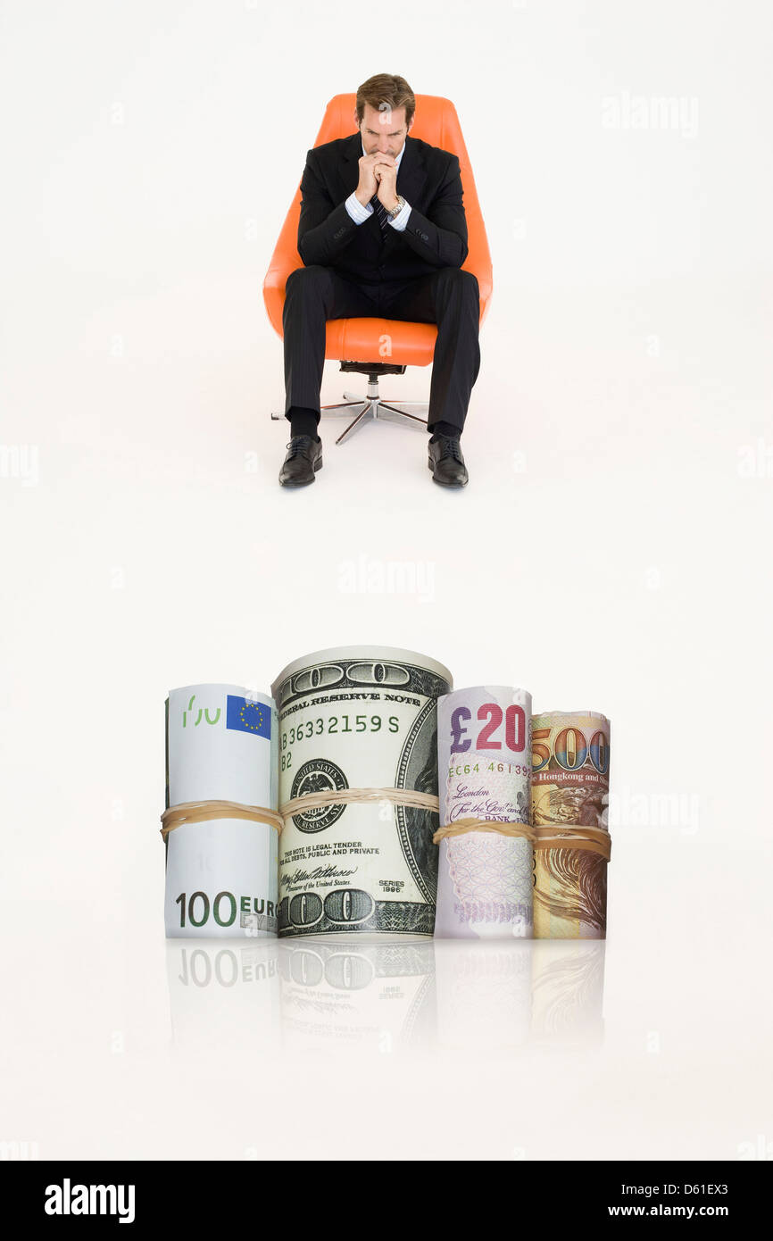 Rotoli di denaro con pensieroso imprenditore sedia che rappresentano problemi finanziari Foto Stock