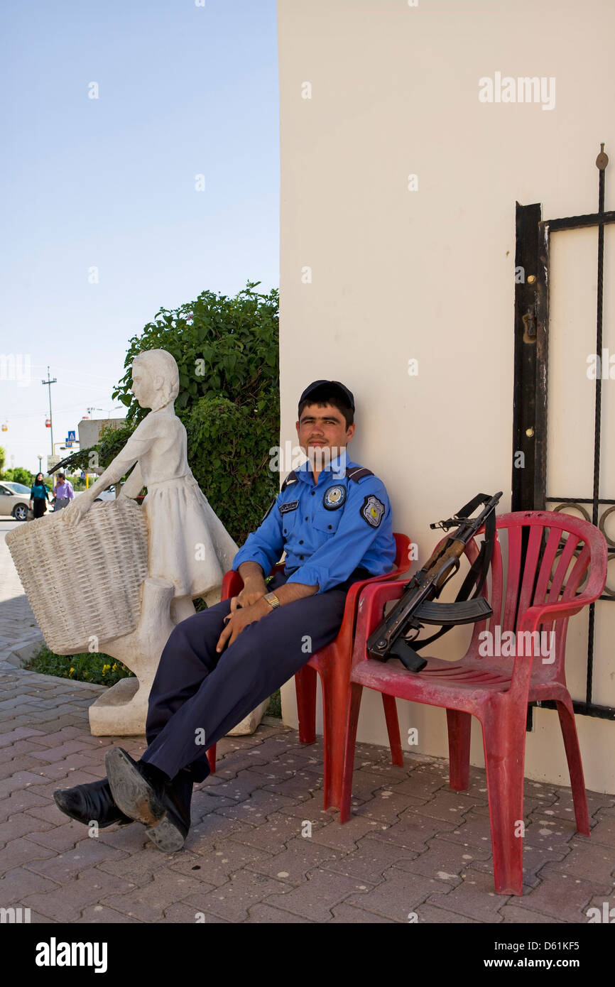 Una guida di sicurezza seduto su una sedia in plastica con il suo fucile accanto a lui a Erbil, Iraq. Foto Stock