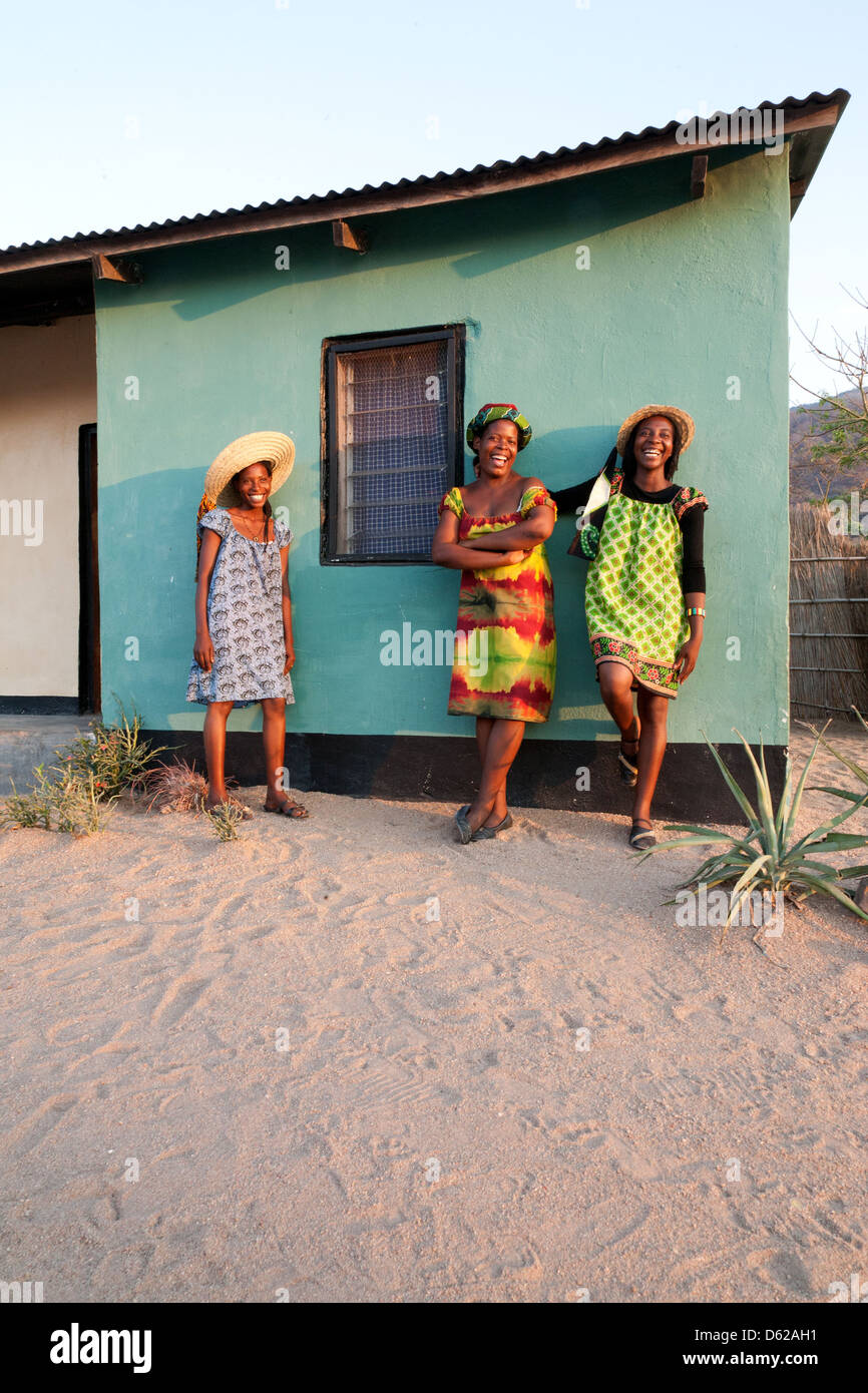 Tre sorridenti signore africani in luminose vestiti contro la parete blu Foto Stock