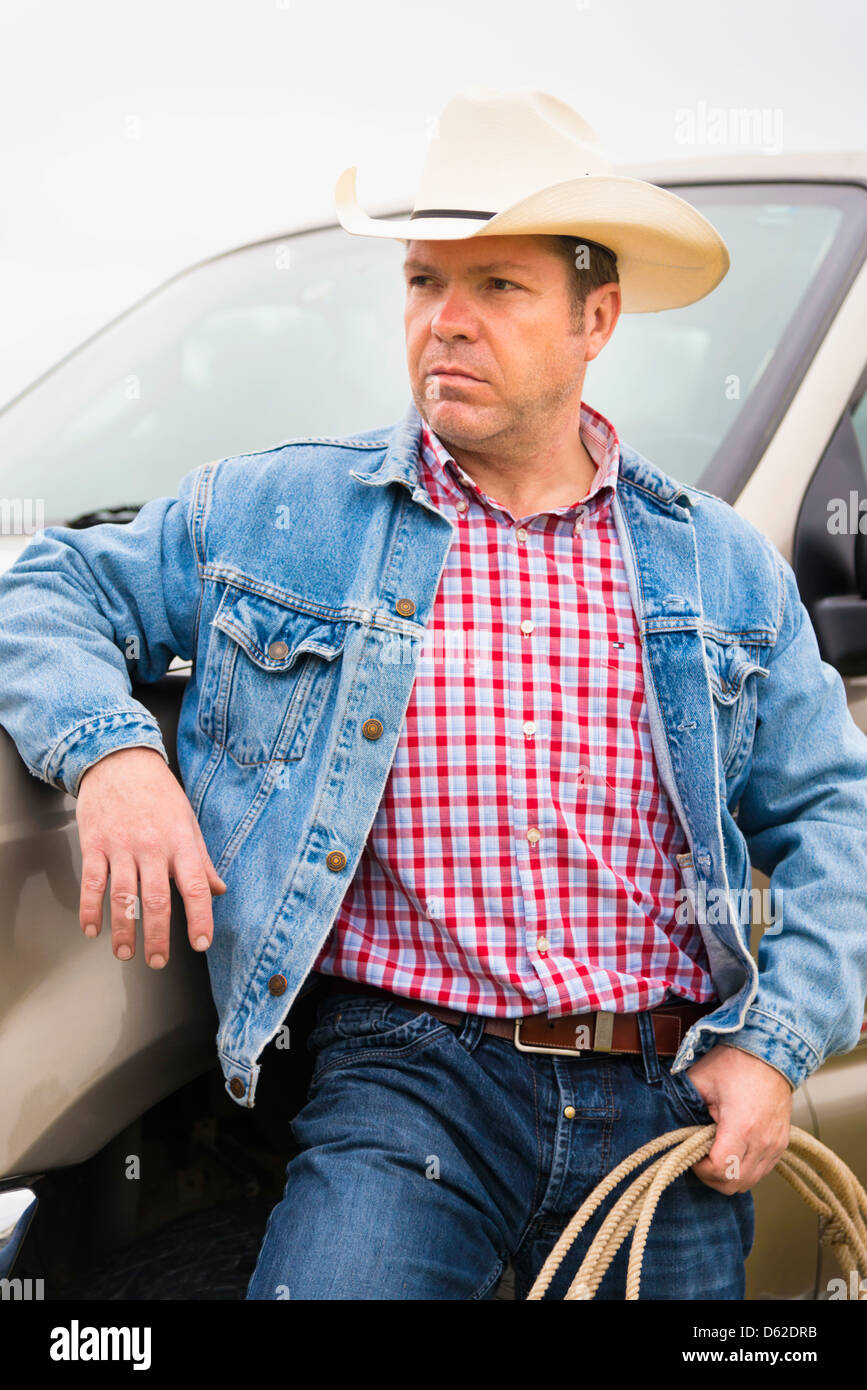Texas Cowboy - di mezza età uomo caucasico di 46 anni con il cappello da cowboy e corda appoggiata contro il carrello di prelievo Foto Stock