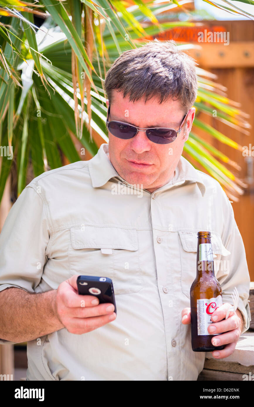 Di mezza età uomo caucasico texting su smart phone in ambiente tropicale Foto Stock