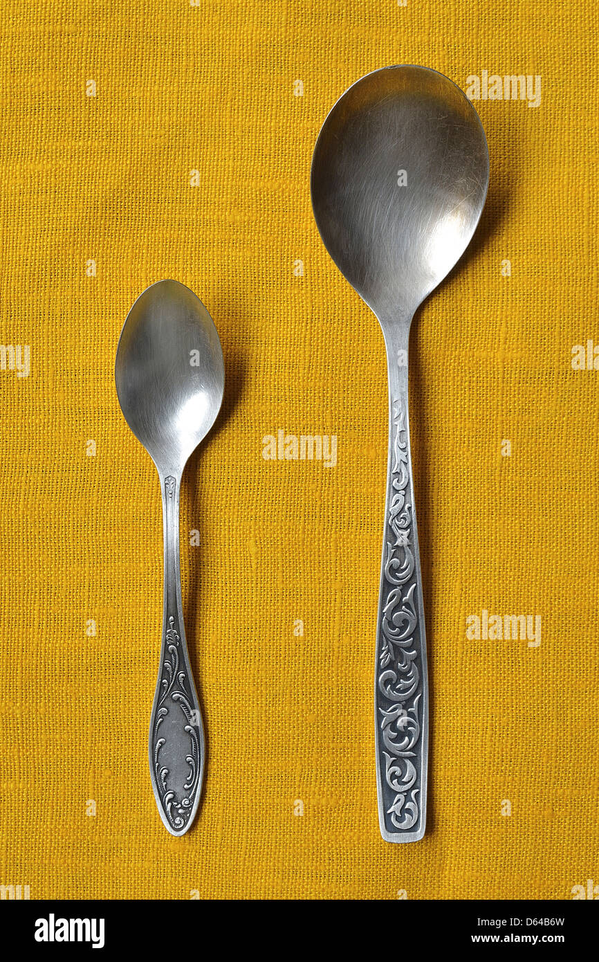 Piccoli e grandi vintage cucchiai di argento sulla tovaglia giallo Foto Stock