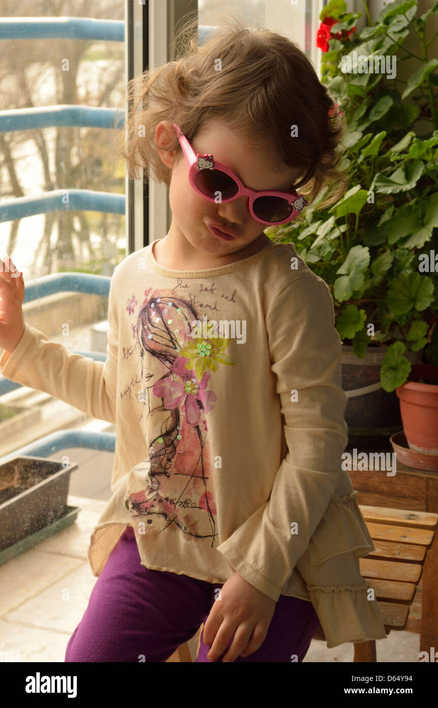 Bambina facendo un sorriso in occhiali da sole seduti in balcone Foto Stock