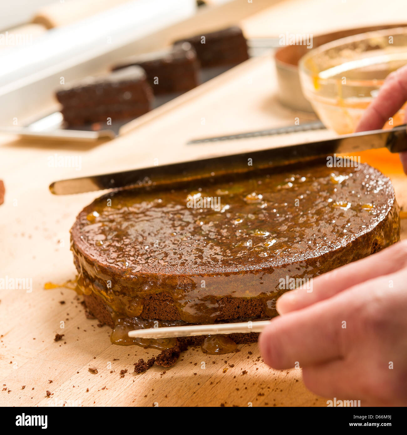 Le mani di Cook in azione diffusione di torta con la marmellata di arance Foto Stock