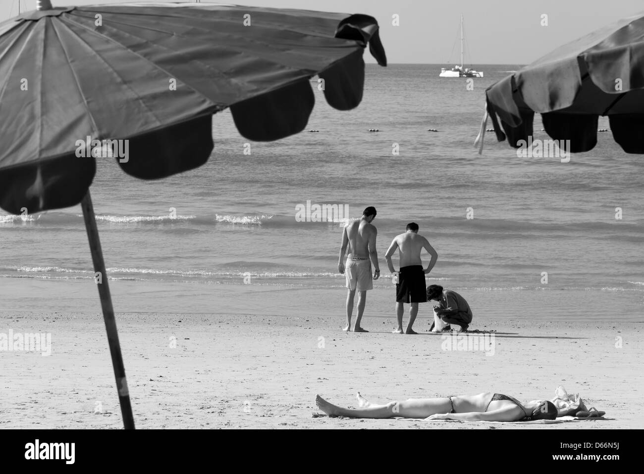 Donna sunbathes sulla spiaggia mentre tre uomini vanno clamming Foto Stock