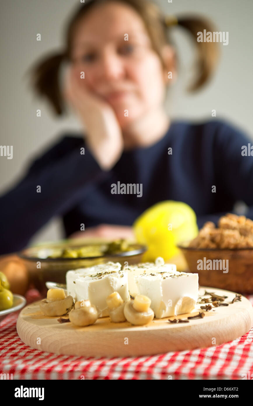 Il formaggio Feta con funghi su un tavolo da cucina. Donna con pig-tail in fuori fuoco sfondo. Foto Stock