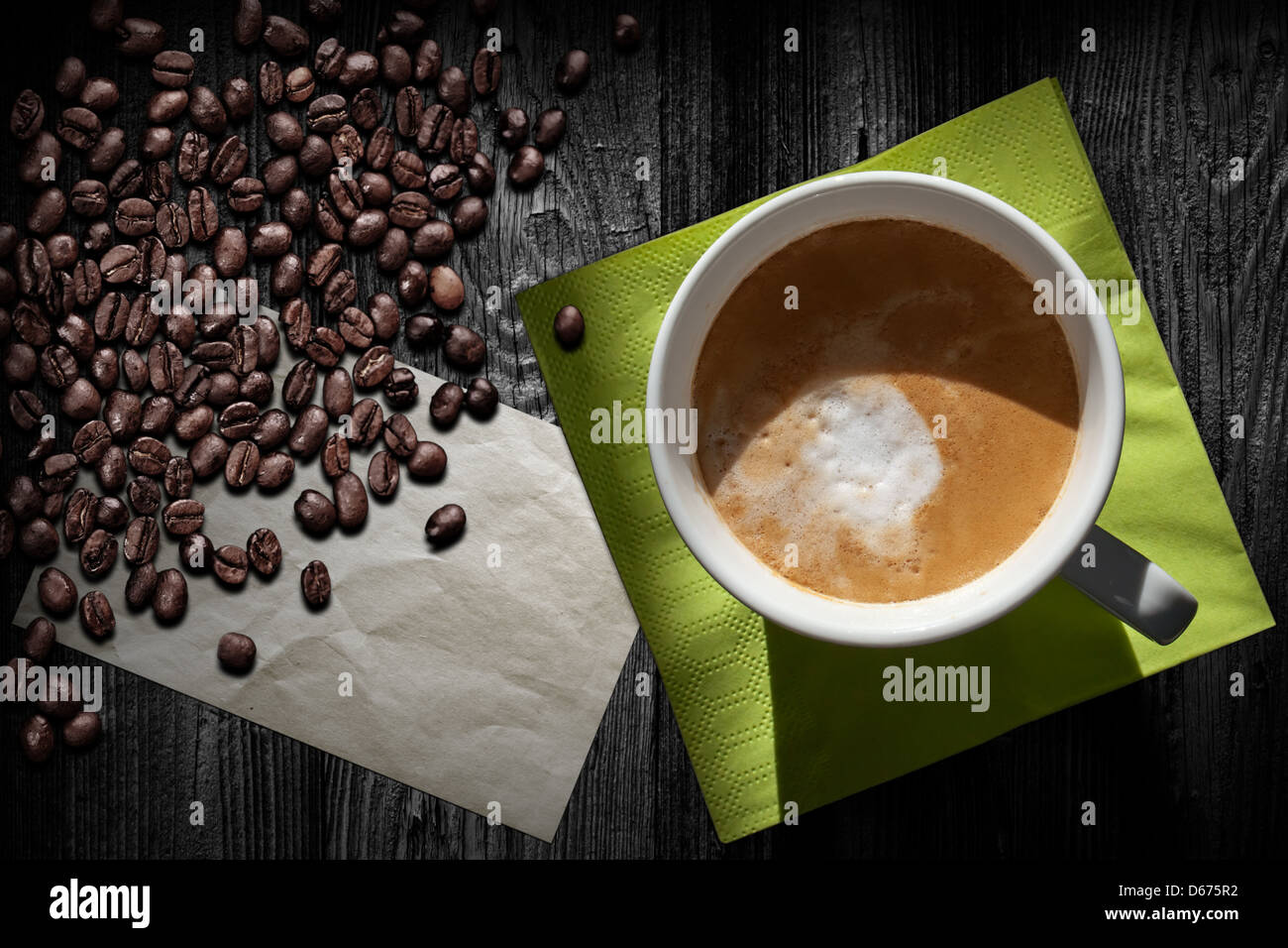 Tazza di cappuccino, caffè vecchio foglio di carta verde, igienico e fagioli su tavoli in legno nero, vista dall'alto Foto Stock