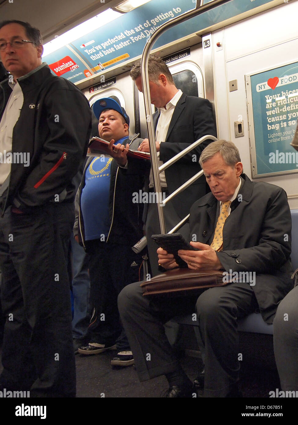 L'uomo leggendo il suo iPad come lui corre in NYC subway assieme al compagno di pendolari, New York, NY, Aprile 11, 2013 © Katharine Andriotis Foto Stock