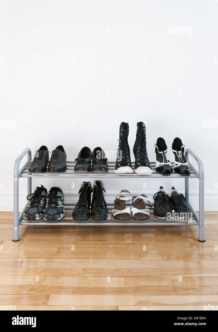 Scarpa rack con nero scarpe e stivali, su un pavimento di legno, oltre ad una parete bianca. Foto Stock