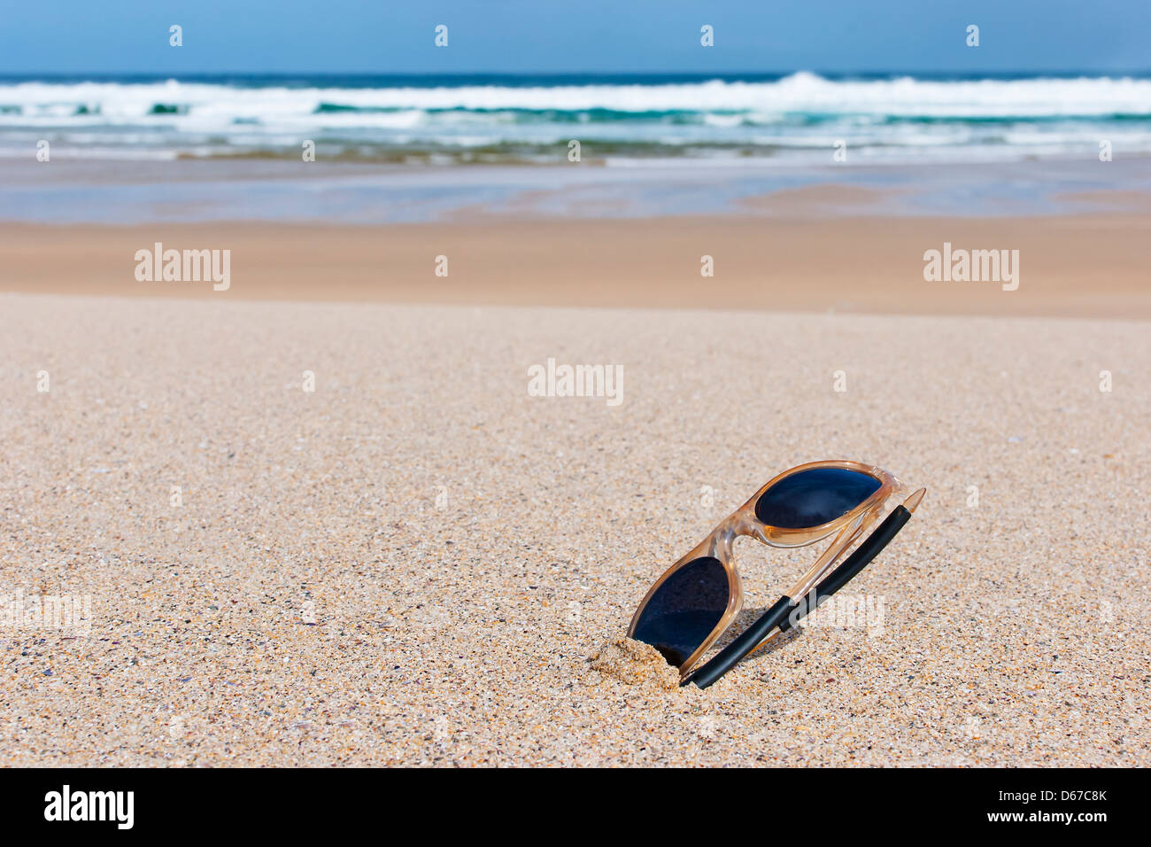 Occhiali da sole sulla sabbia di una spiaggia solitaria Foto Stock
