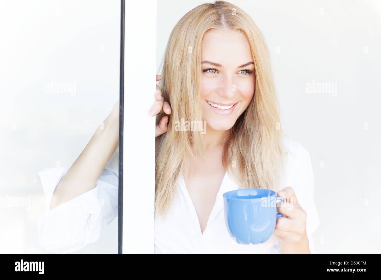 Splendida donna sorridente in piedi vicino alla finestra aperta a casa e godere di una gustosa bevanda caffè del mattino, il concetto di felicità Foto Stock