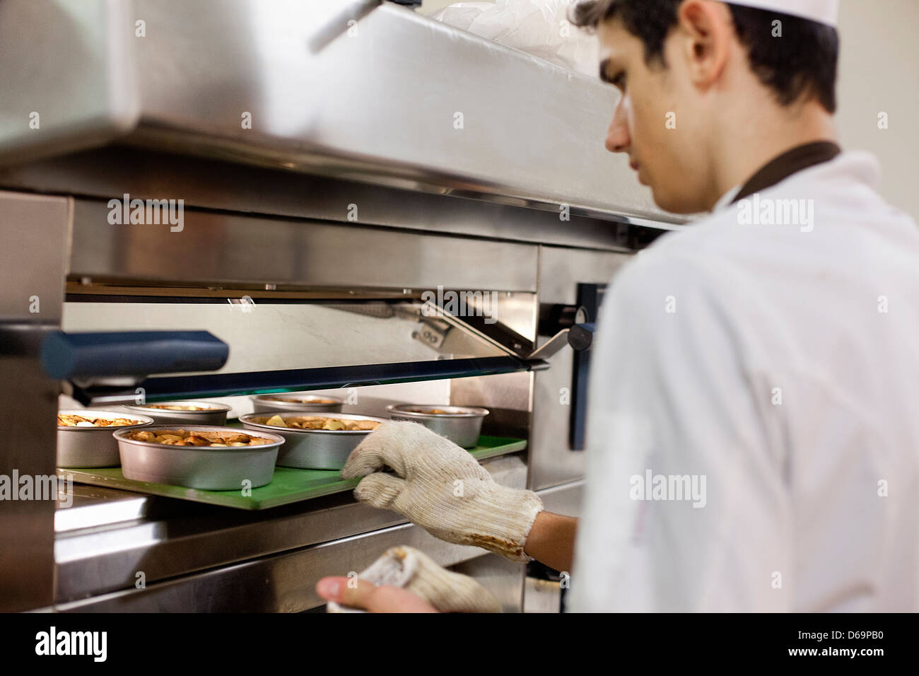Baker mettendo il cibo nel forno in cucina Foto Stock