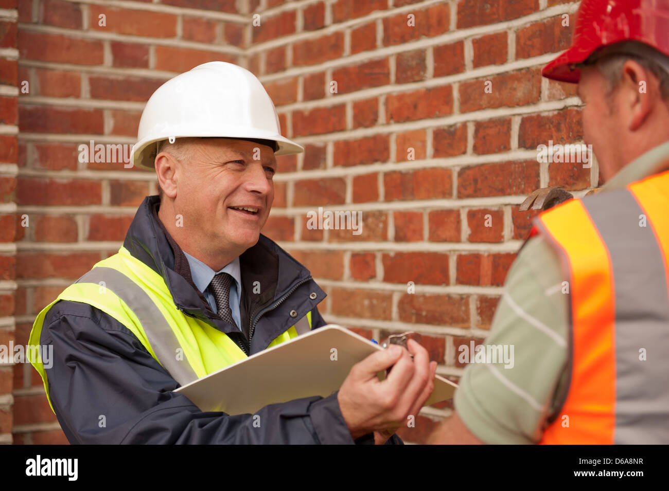 Ispettore di costruzione/caposquadra parlando di operaio mentre scrivere le note. Foto Stock